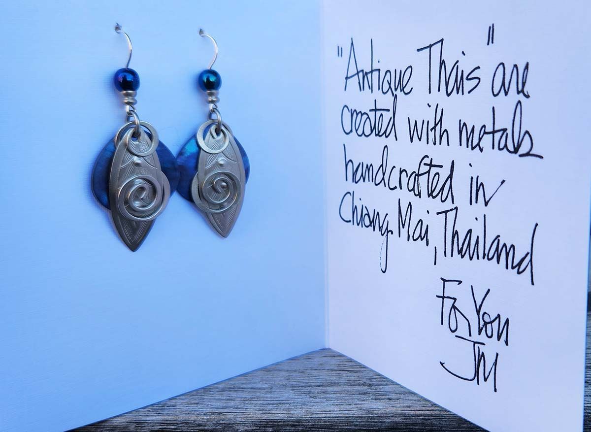 A pair of earrings sitting on a table next to a card that says fortune thais are created with metals