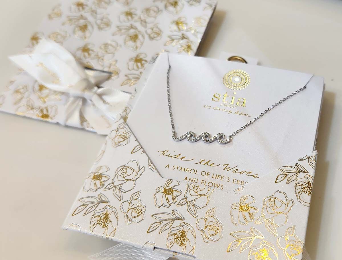 A necklace is in a white box with gold foil