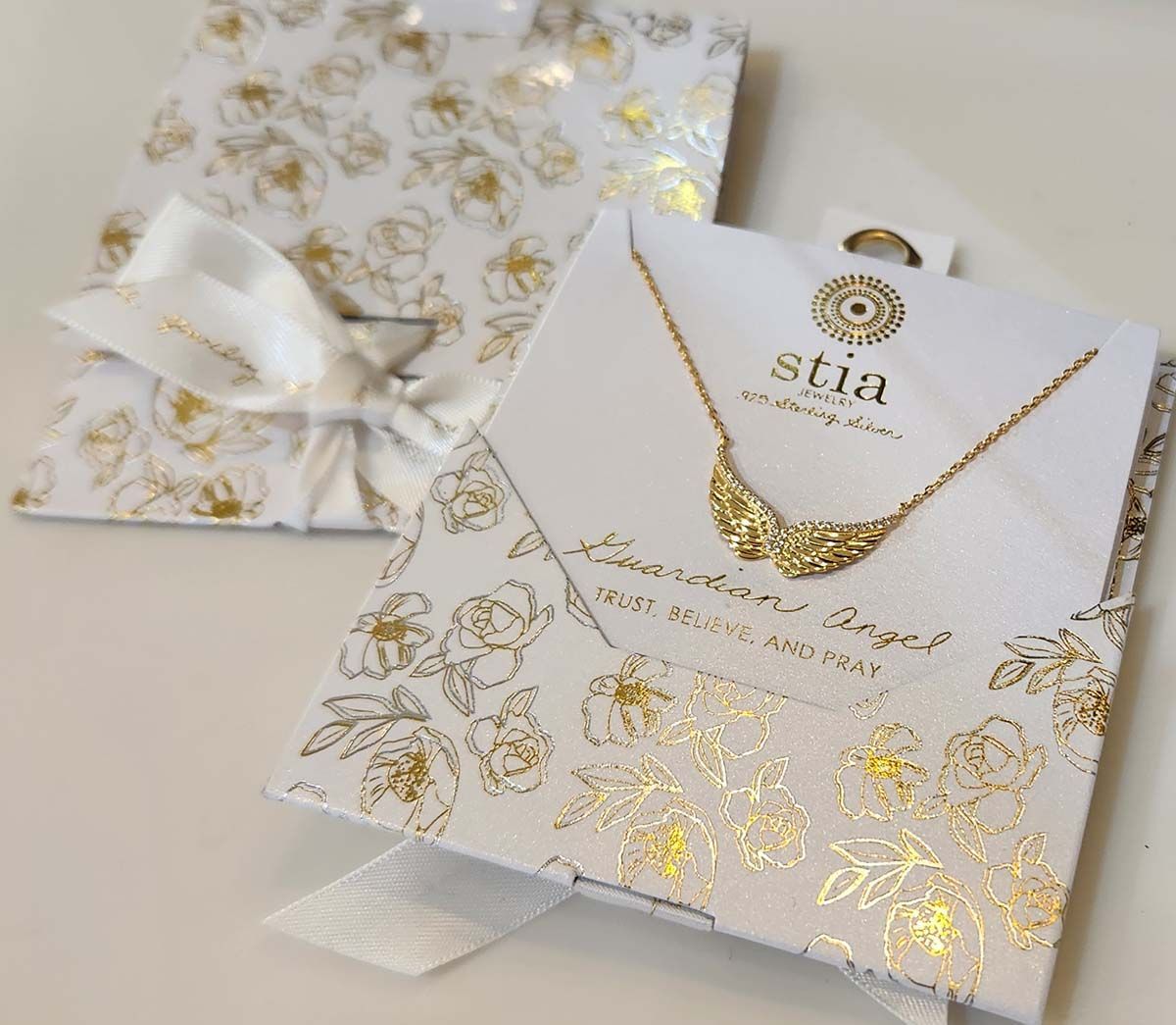 A gold necklace in a white box with the word stia on it