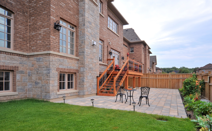 A photo of a backyard second-level deck. This is a beautiful deck with stairs leading down to a patio in their backyard. The deck is a burnt orange color and has black railings. Looks very good.