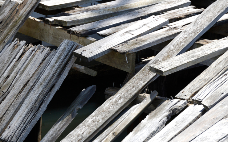A photo of an old broken deck in desperate need of repair. The deck boards are warped, broken, missing, and rotted.