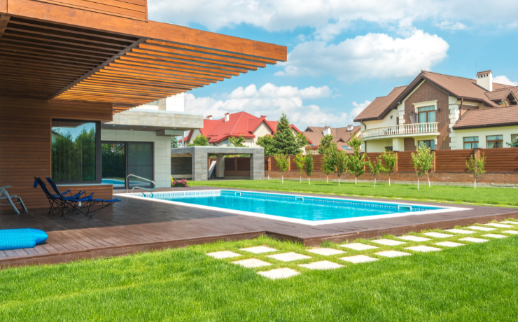 A photo of a luxurious pool deck built by Blue Buffalo Decks. The pool deck surrounds the pool. The backyard is enclosed with a fence.