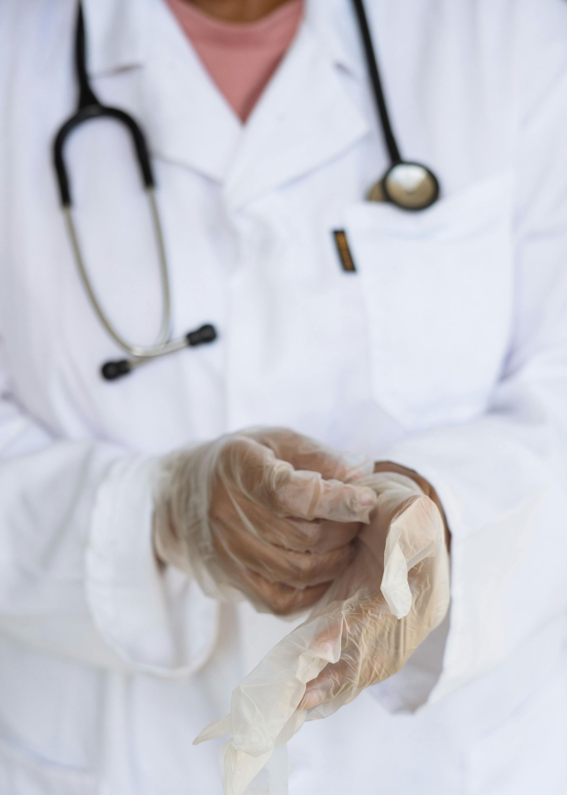 Doctor putting on medical gloves, wearing a white coat and stethoscope.