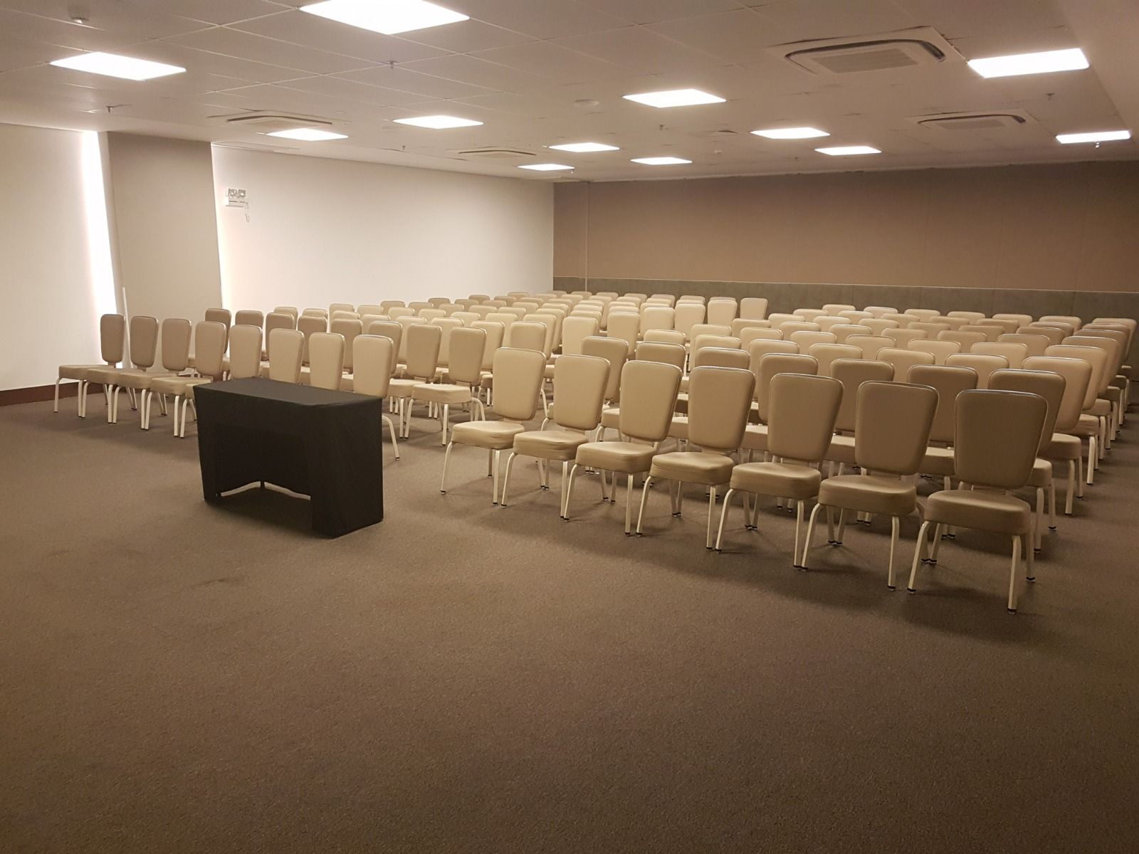 Uma grande sala cheia de fileiras de cadeiras e uma mesa.