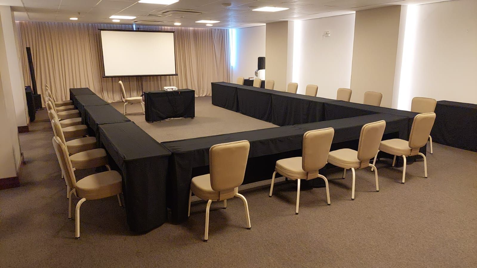 Uma sala de conferências com mesas e cadeiras e uma tela de projeção.
