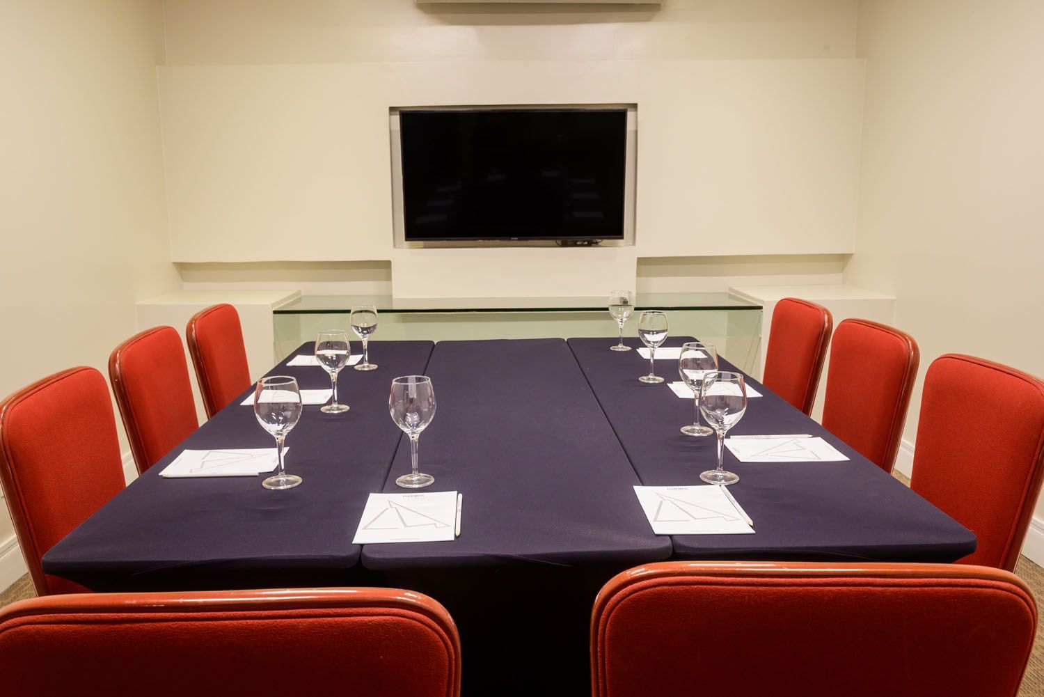 Uma sala de conferências com uma longa mesa e cadeiras vermelhas.