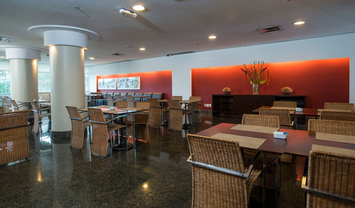 Um restaurante com mesas e cadeiras e uma parede vermelha.