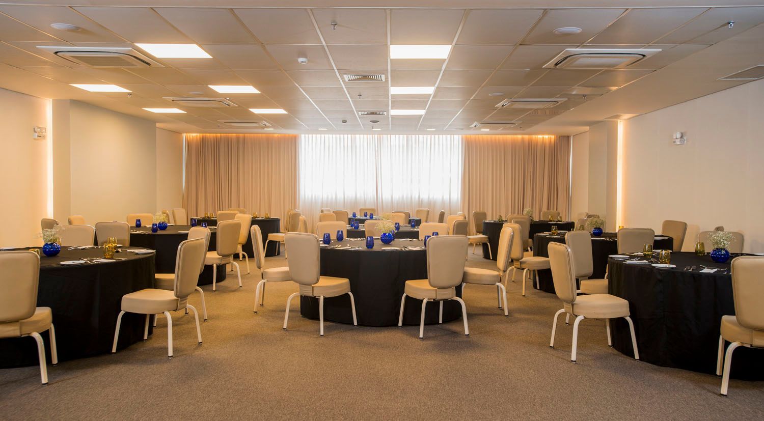 Uma grande sala com mesas e cadeiras preparadas para uma reunião.