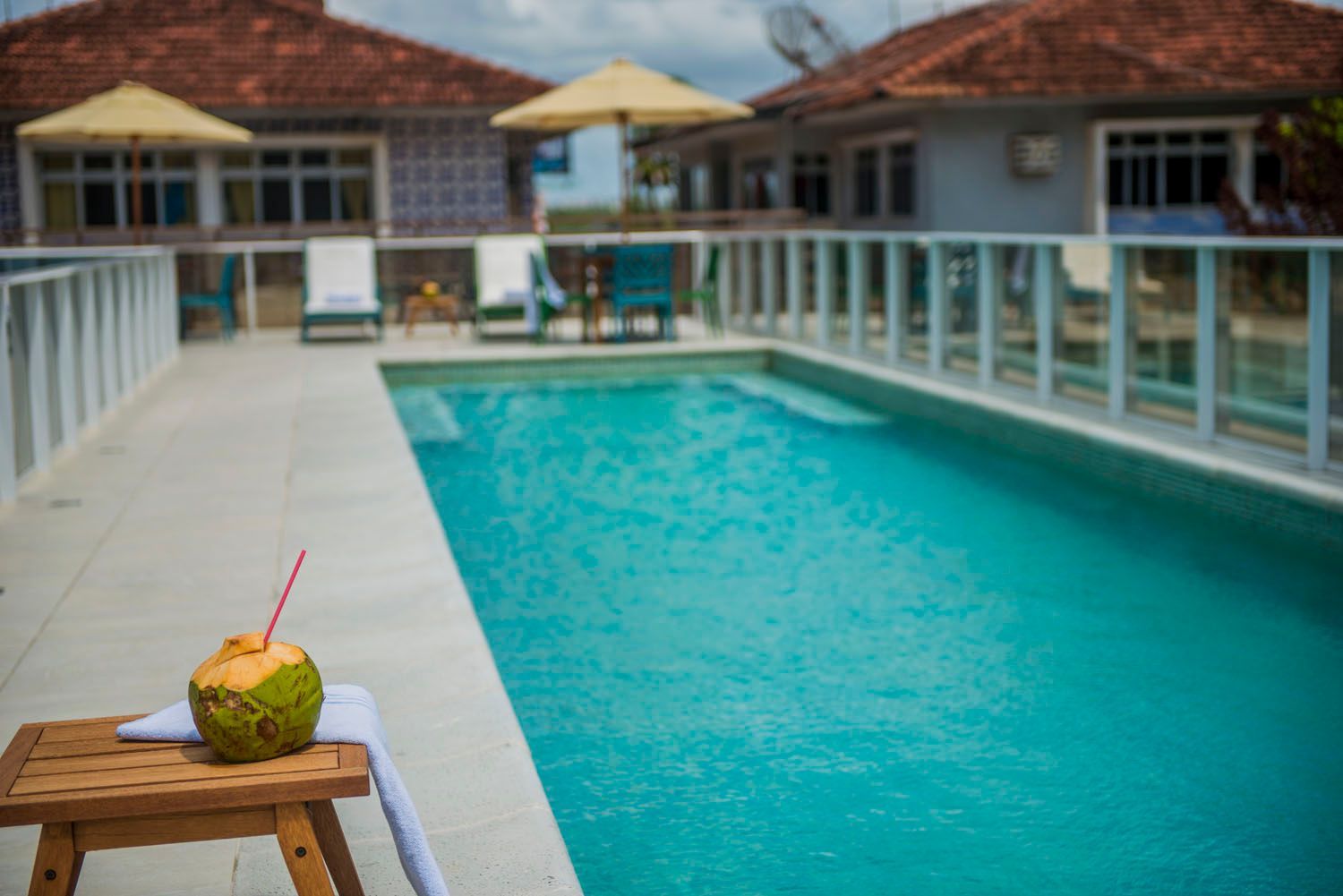 Um coco com canudo está sobre uma mesa de madeira ao lado de uma piscina.