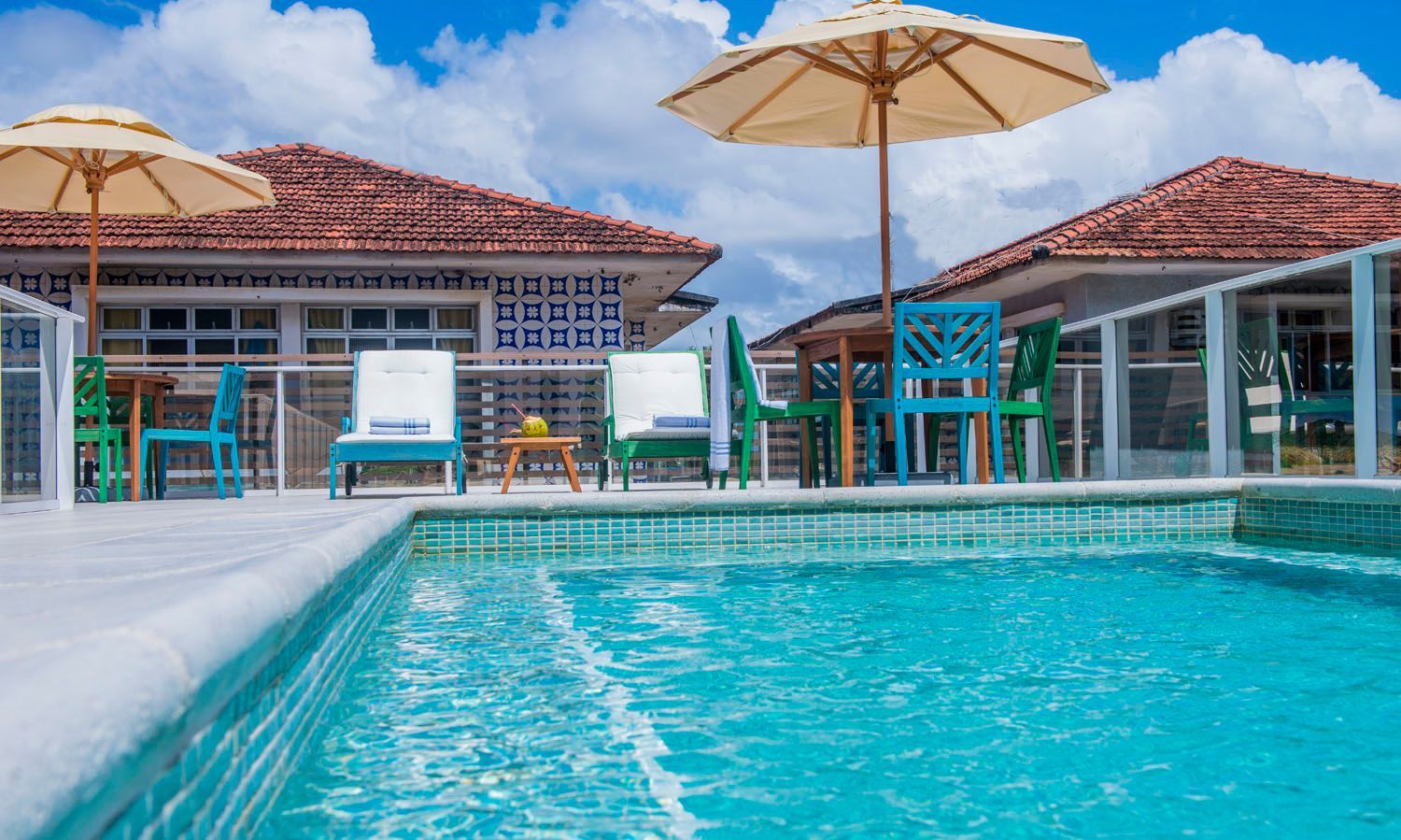 Uma piscina com cadeiras e guarda-sóis em frente a uma casa.