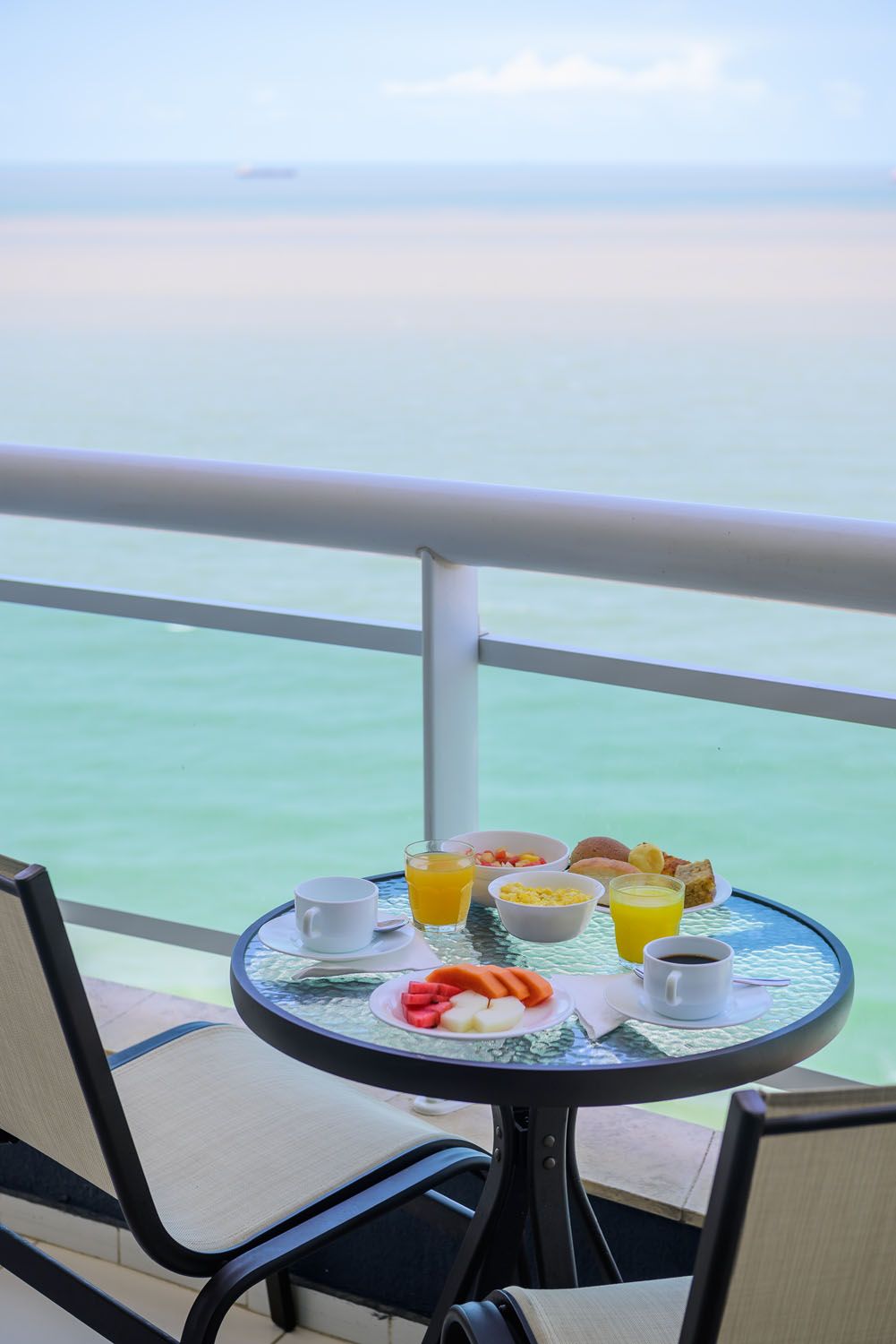 Uma mesa com comida fica em uma varanda com vista para o oceano.