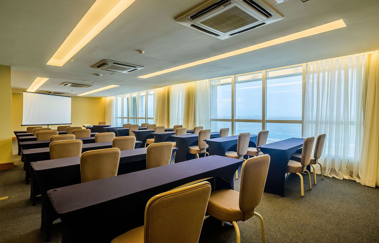 Uma sala de conferências com mesas e cadeiras e uma tela de projeção.