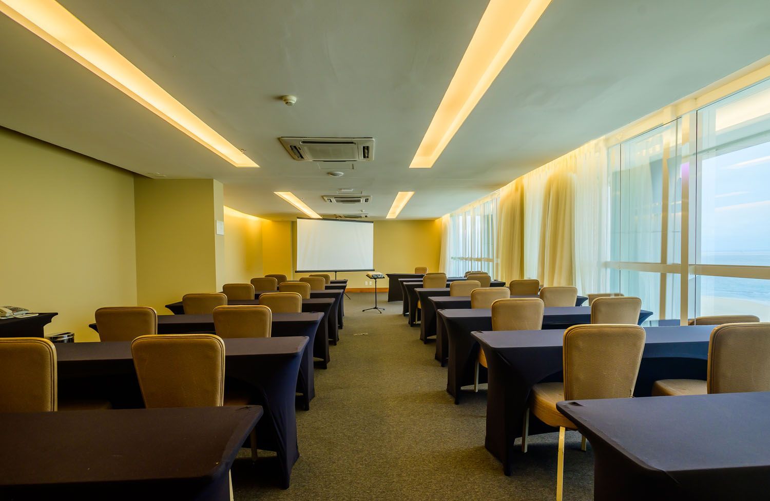 Uma sala de conferências com mesas e cadeiras e uma tela de projeção.