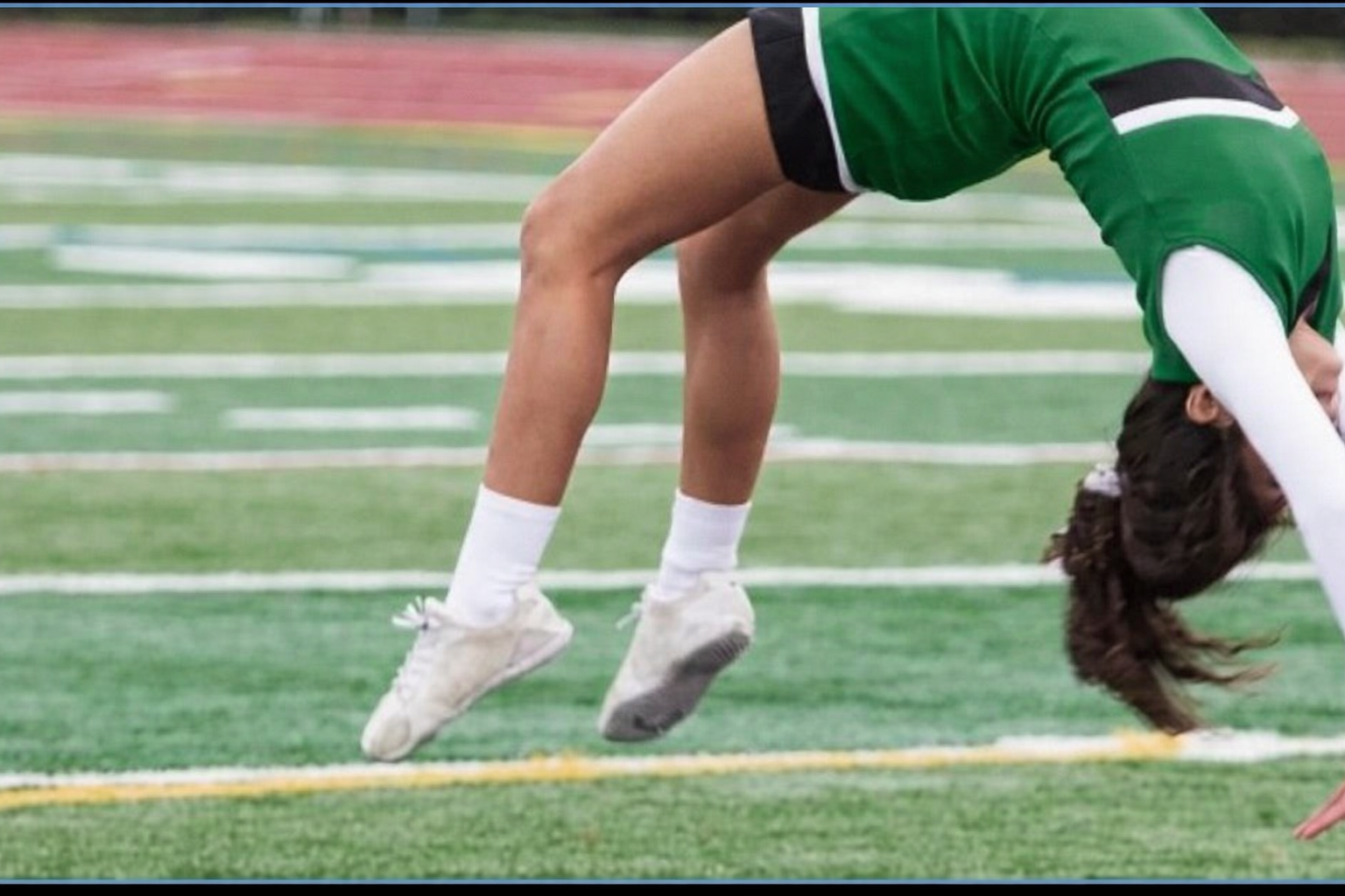 Cheerleader in red uniform performs a backbend on a green and red football field.