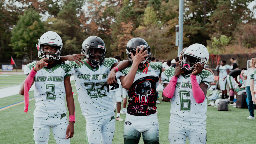 Football players huddle around a football, reaching hands together, blue sky backdrop.