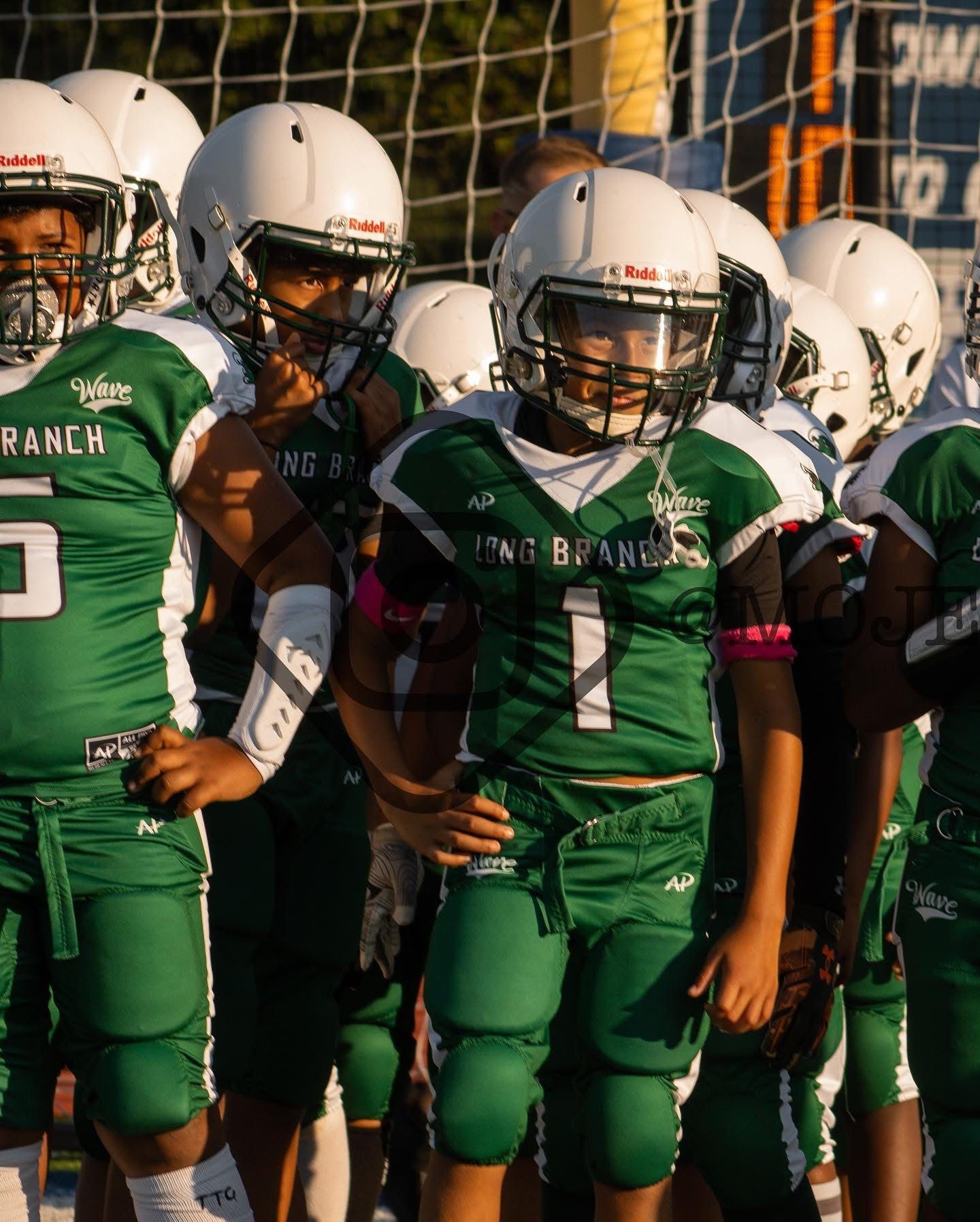 Football players in action on a grassy field; one runs with the ball, pursued by two opponents.