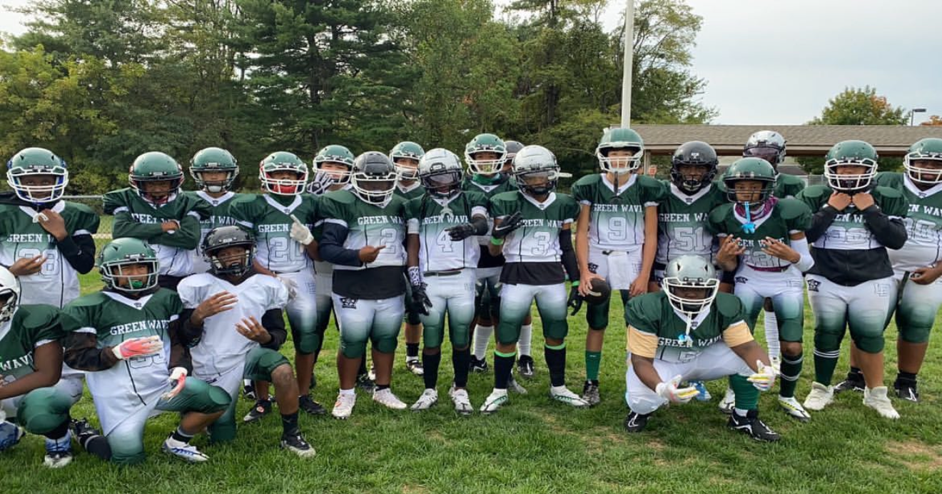 Football player in silver uniform runs with ball on a green field.