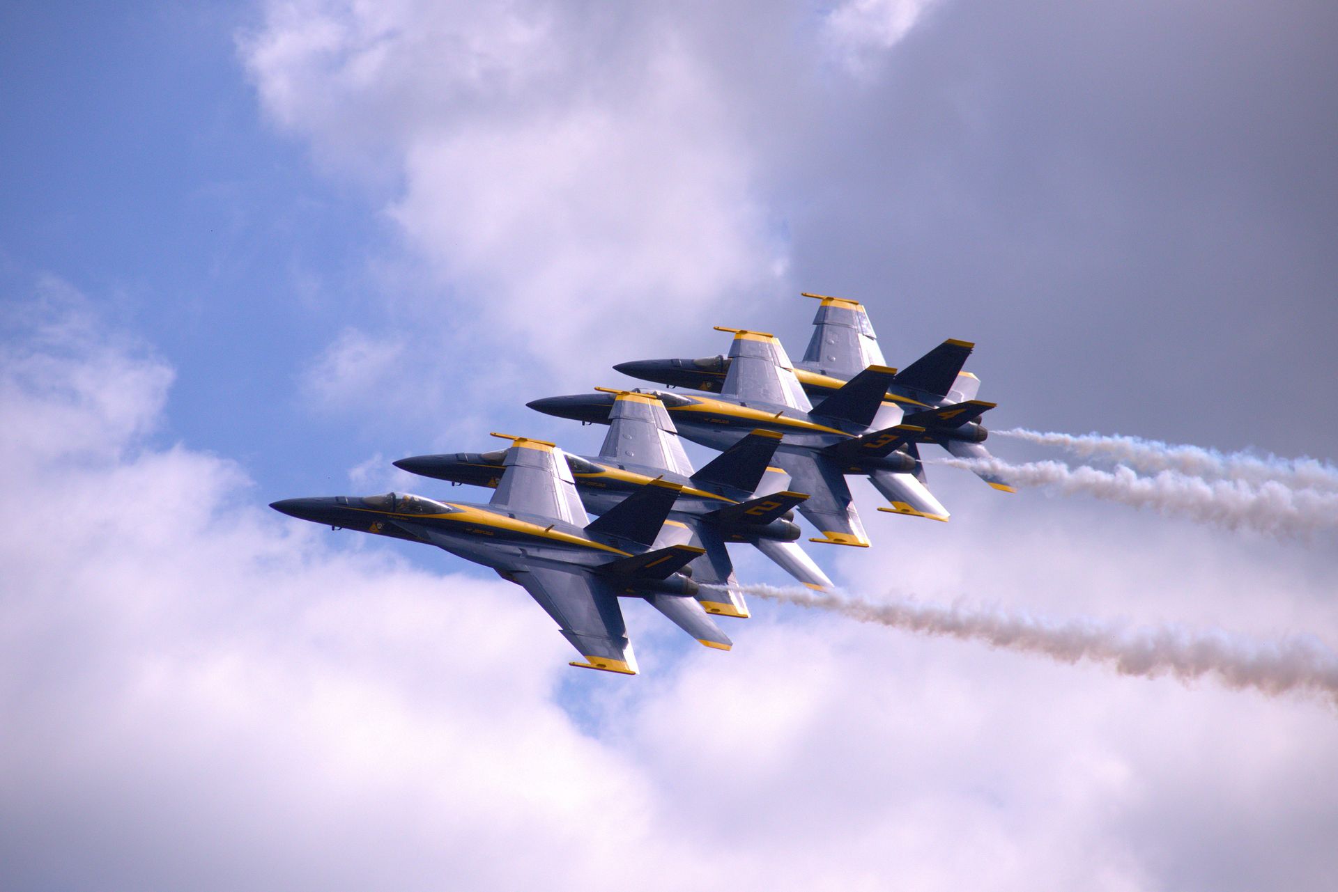 Blue Angels flying in formation against a cloudy sky, trailing white smoke.