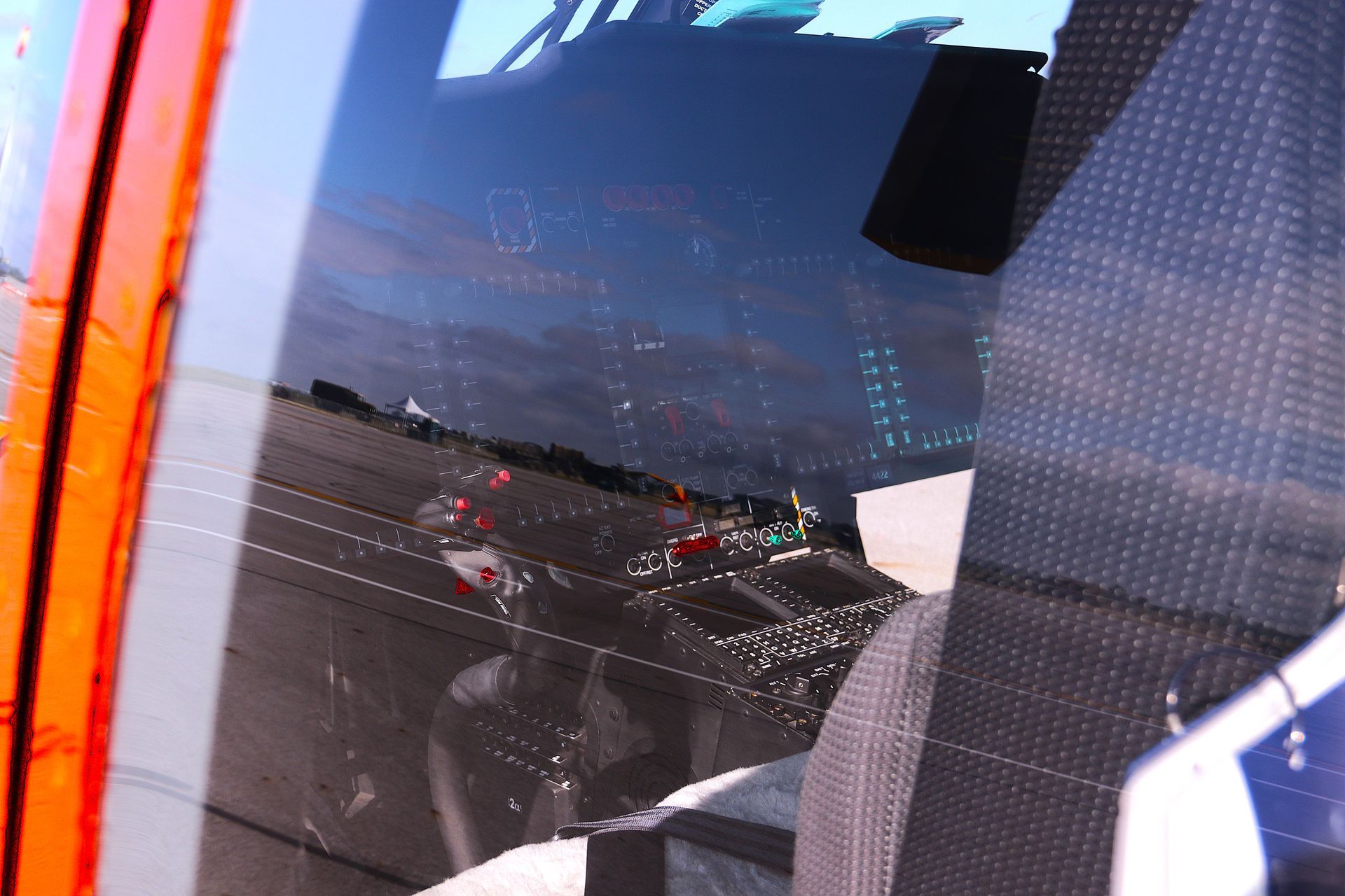 Reflection in airplane window; runway and other planes are visible.