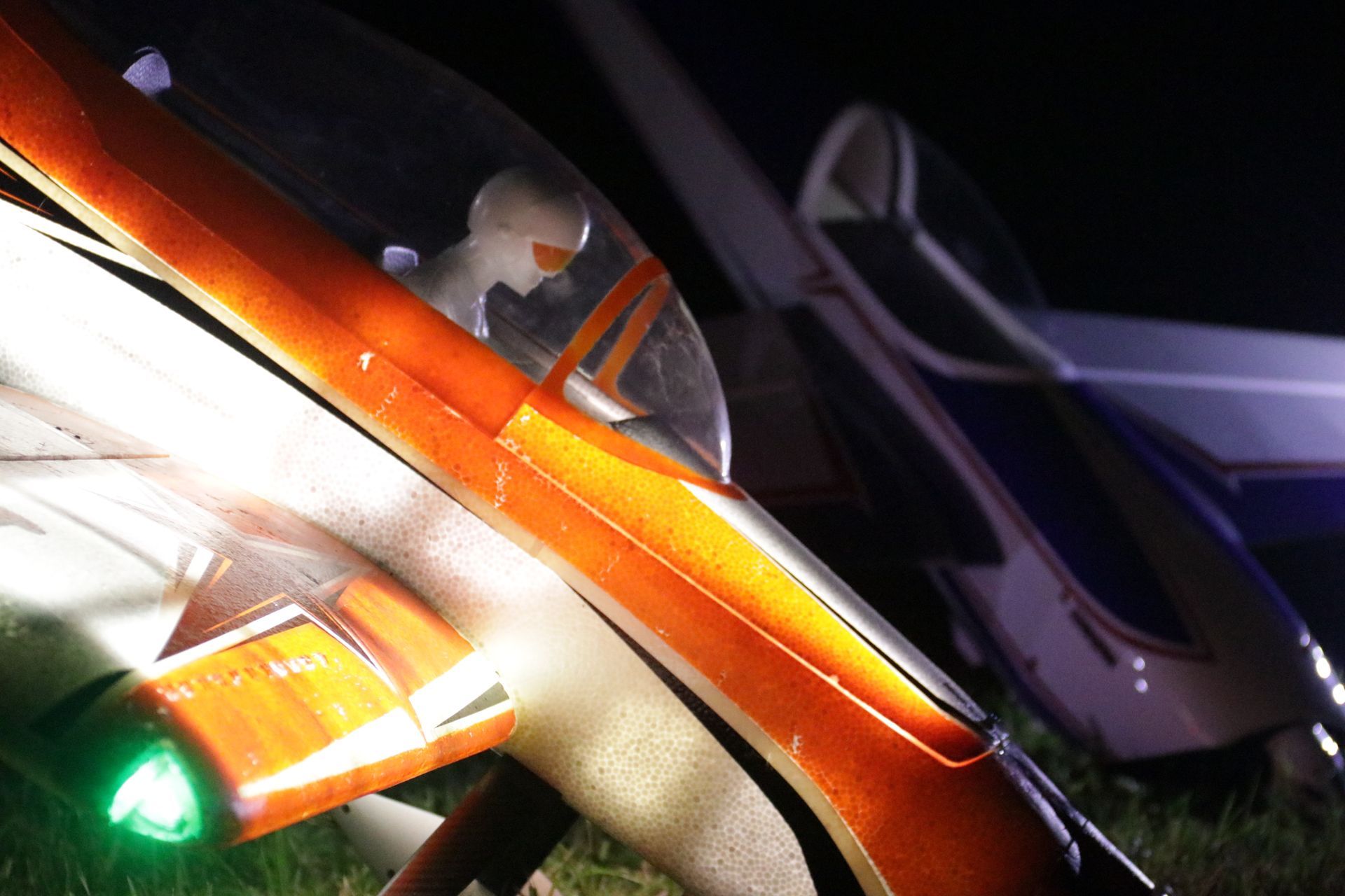 Orange and white small airplane with a pilot in the cockpit, parked at night.