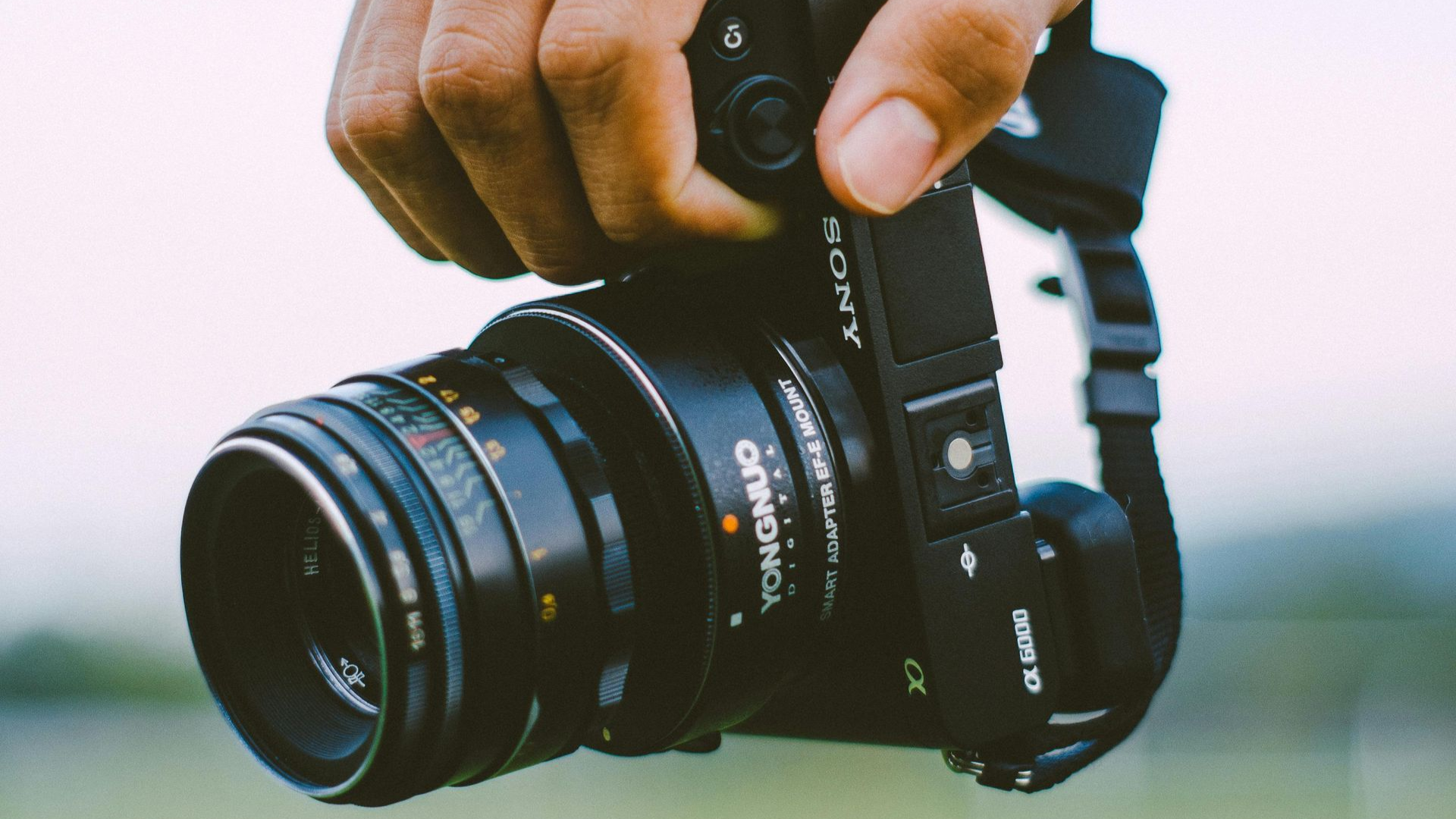 Hand holding a black camera with a lens, outdoors.