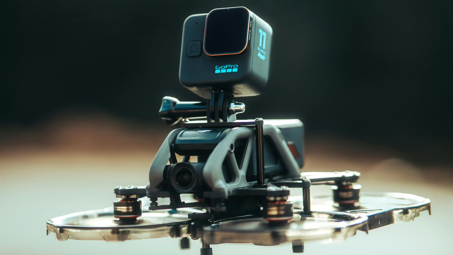 A black drone with a mounted GoPro camera, against a blurred background.