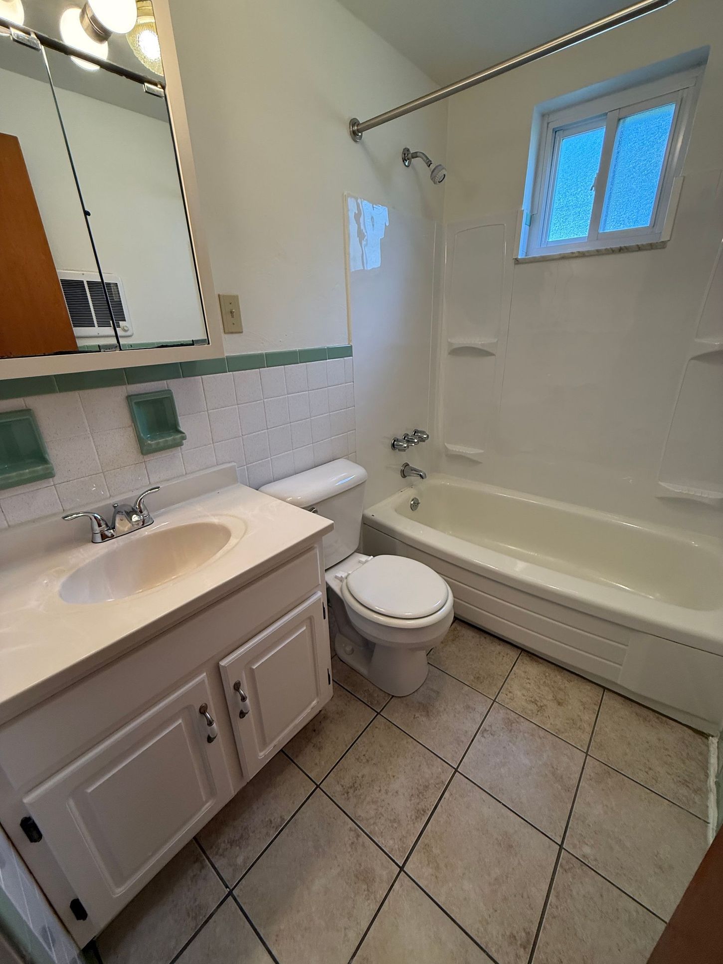 Bathroom with white vanity, toilet, tub, and small window. Beige diamond-patterned tile floor.
