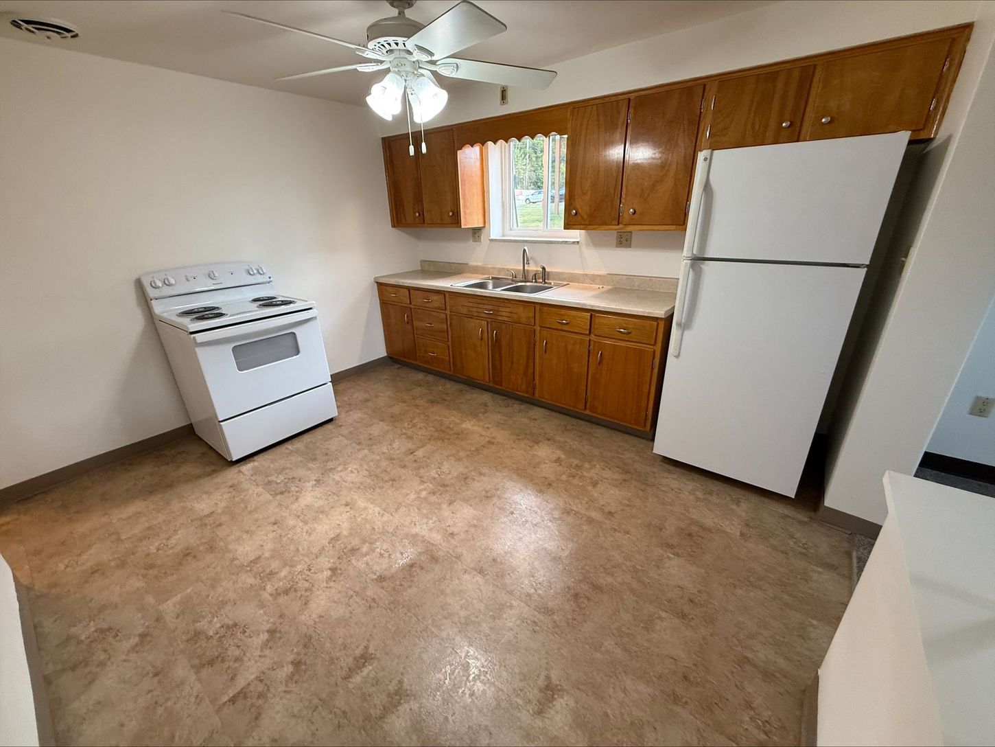 Kitchen with white appliances, brown cabinets, and tan flooring. A ceiling fan hangs above.