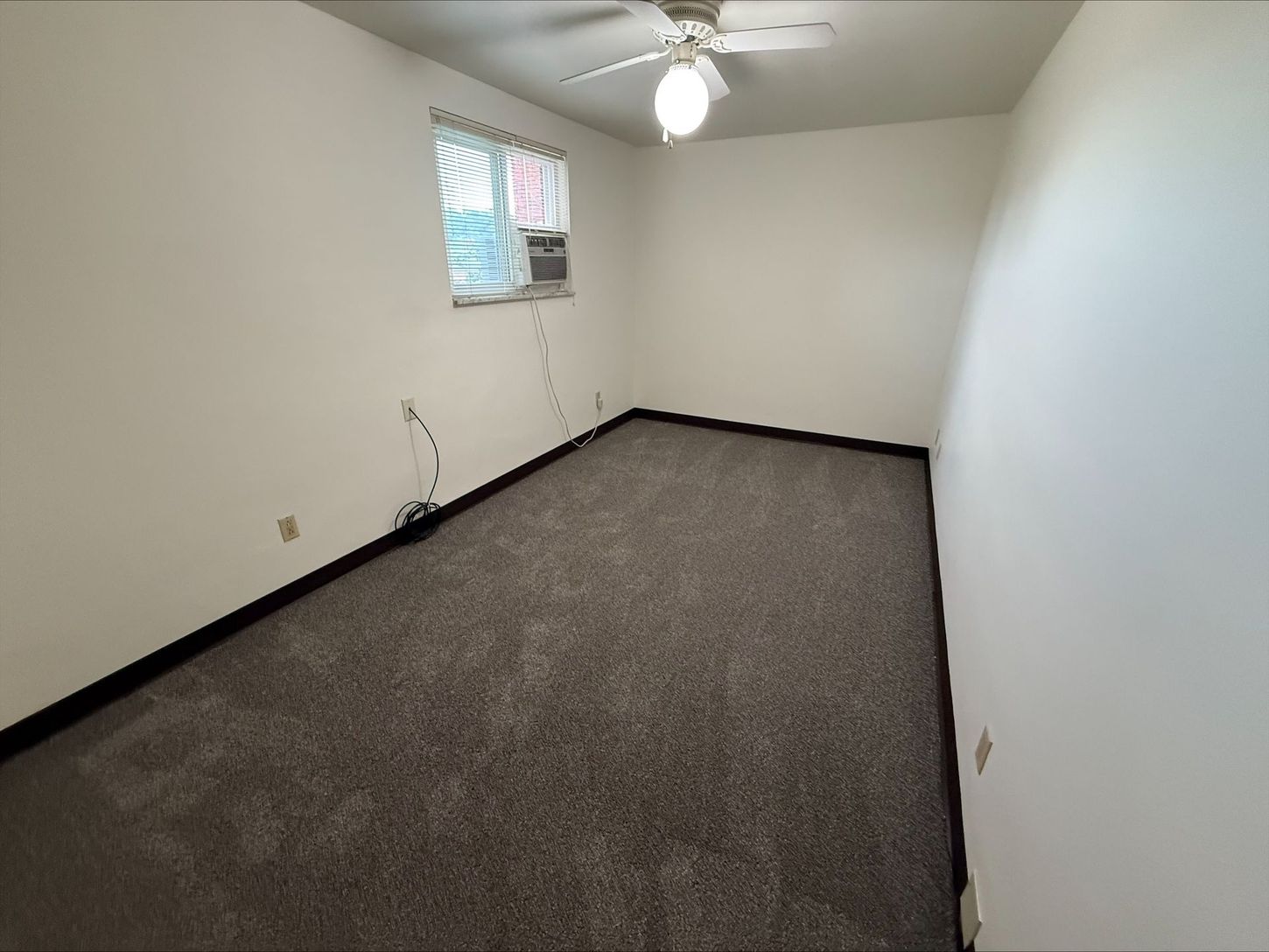 Empty room with gray carpet, white walls, and a window with a small air conditioner.
