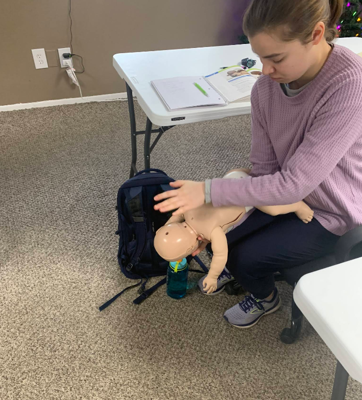 Woman practicing infant CPR on a training dummy, indoors.
