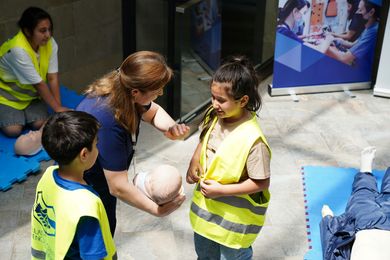 Children and adults in vests practice CPR on dummies. Indoors.