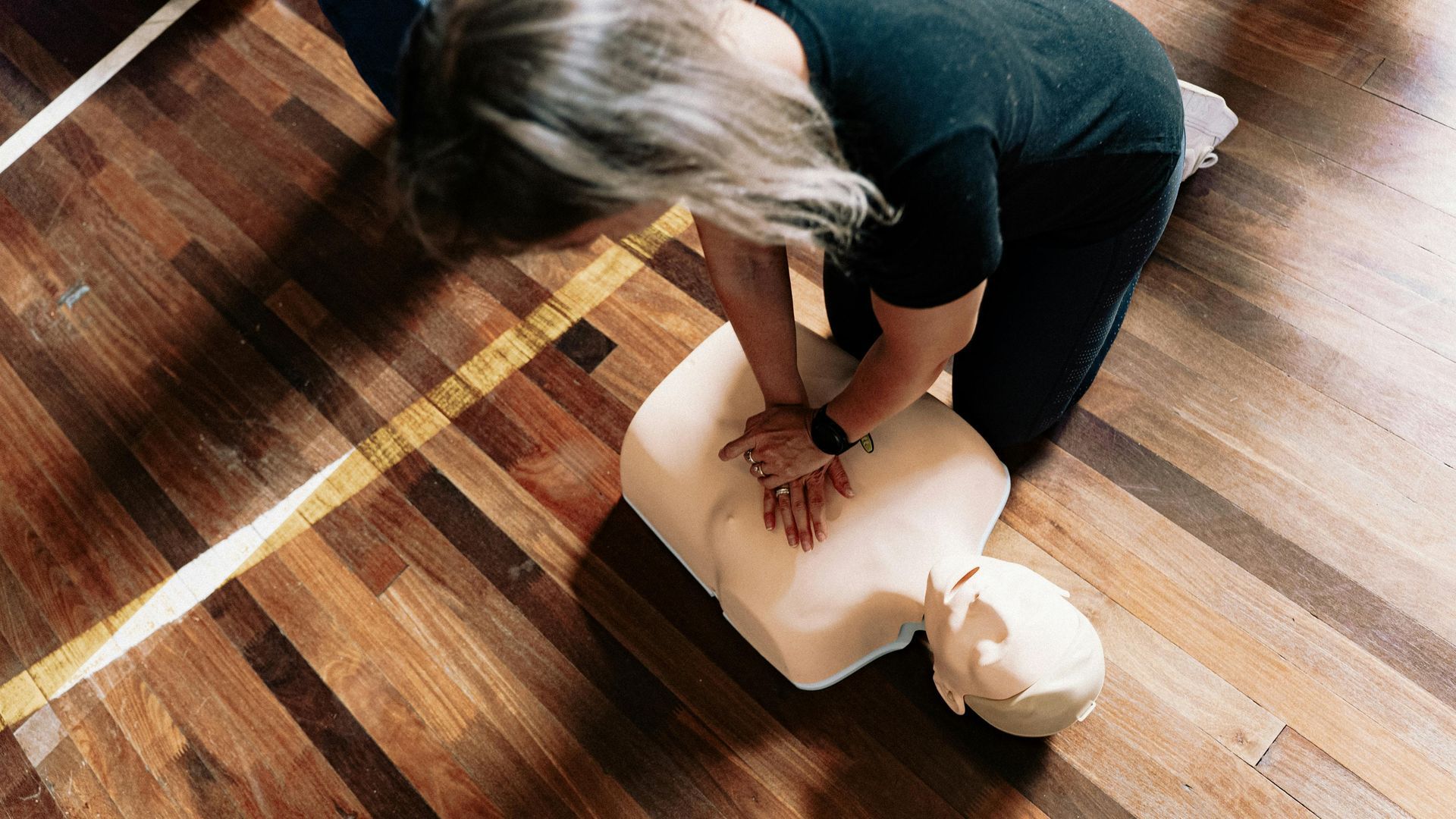 Person performing CPR on a mannequin in a room with wood flooring.