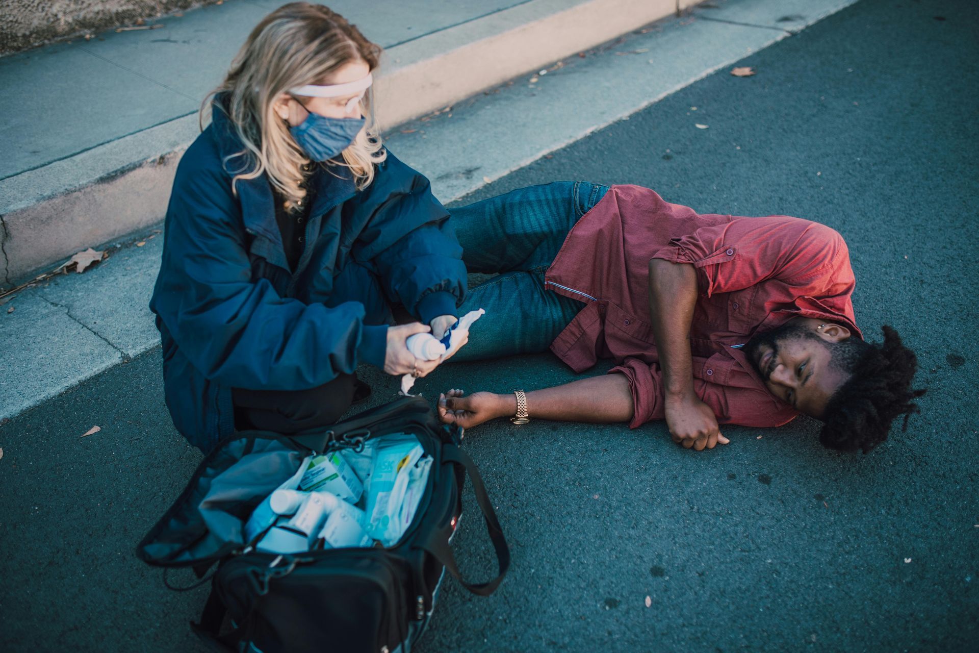 Woman in mask treating injured man on the street.