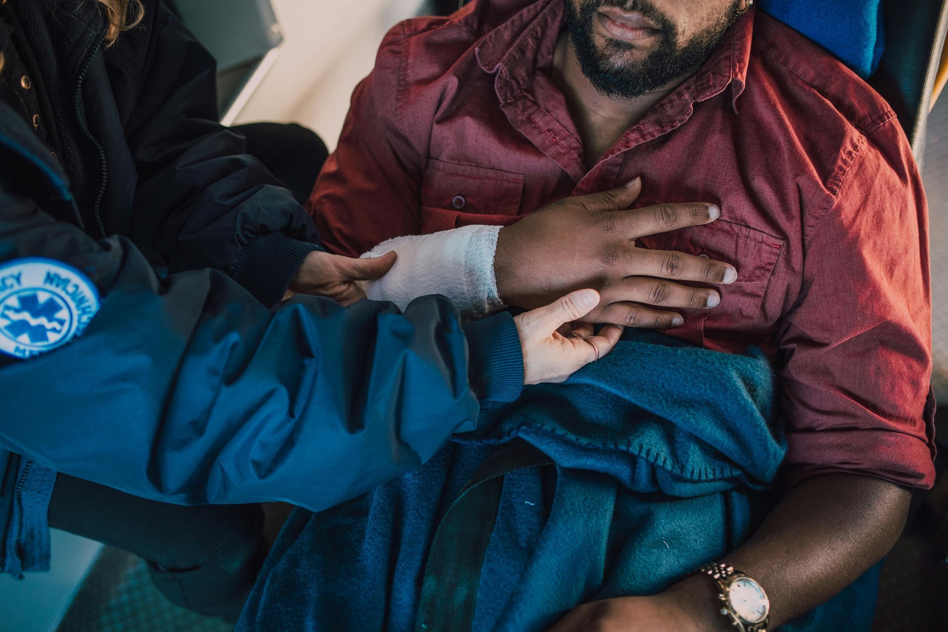 Man in ambulance with bandaged wrist and chest pain, receiving medical attention.