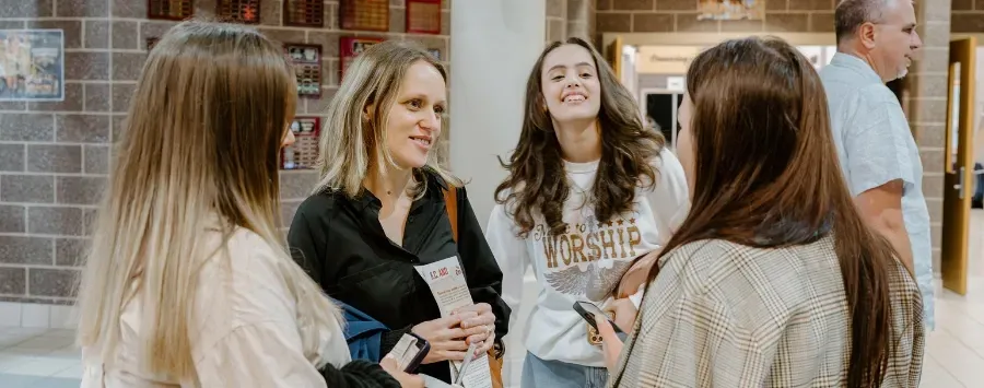 A group of women are standing in a hallway talking to each other.