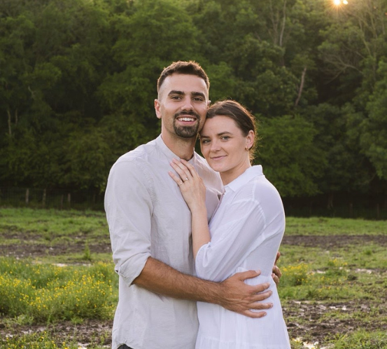 A man and a woman are posing for a picture in a field.