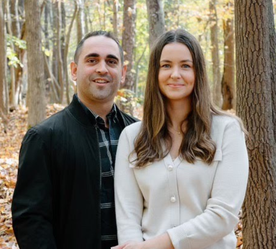 A man and a woman are posing for a picture in the woods