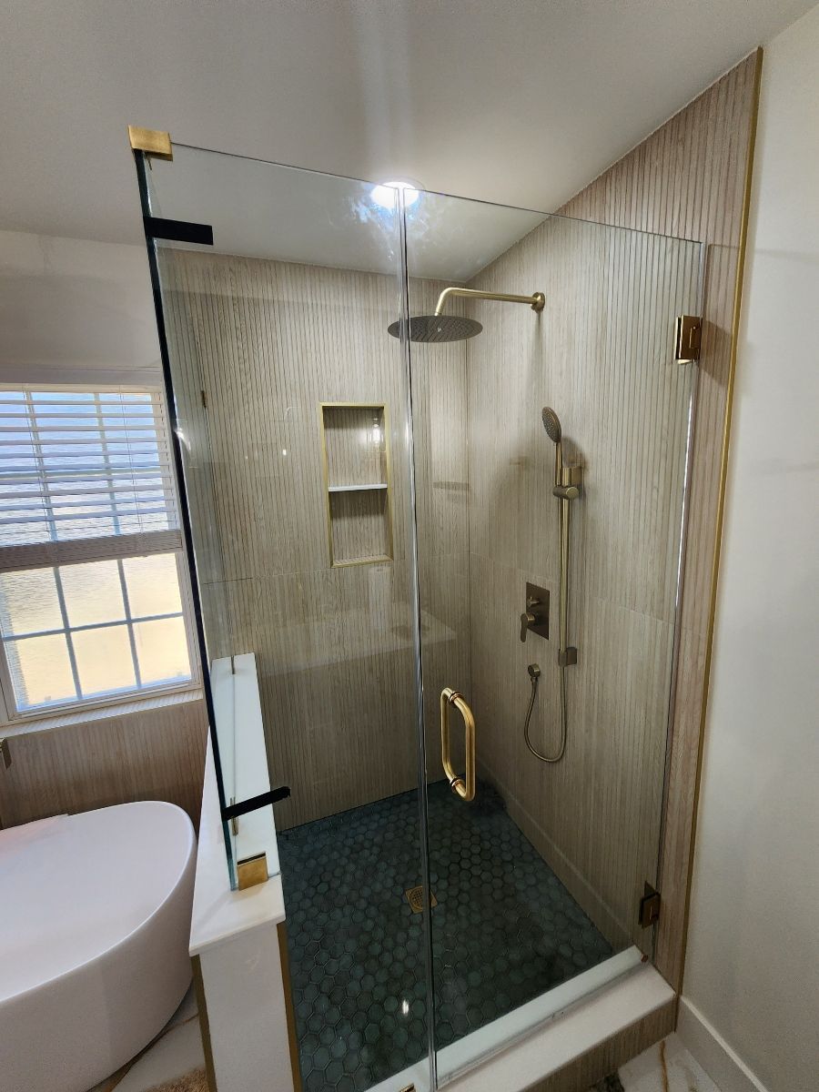 Modern shower with glass door, gold fixtures, and mosaic floor tiles.