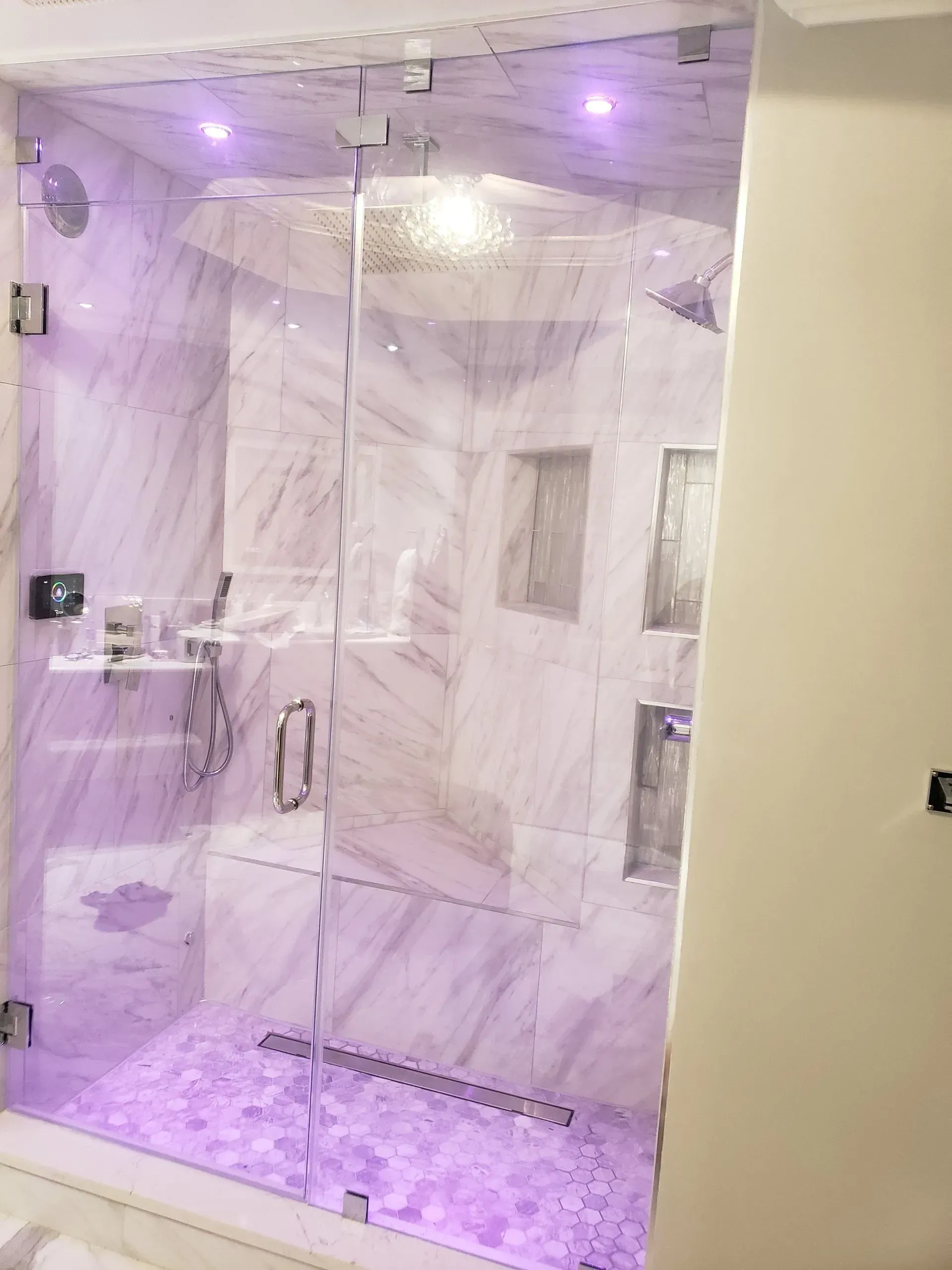 A bathroom with a glass shower door and purple lights.