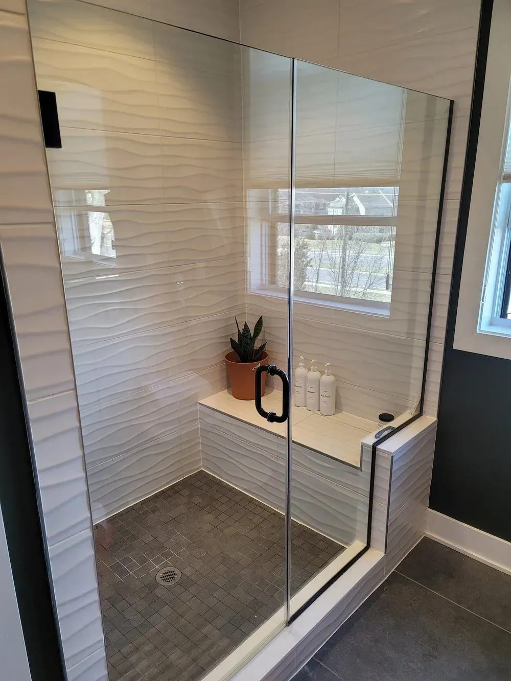 A bathroom with a glass shower door and a bench.