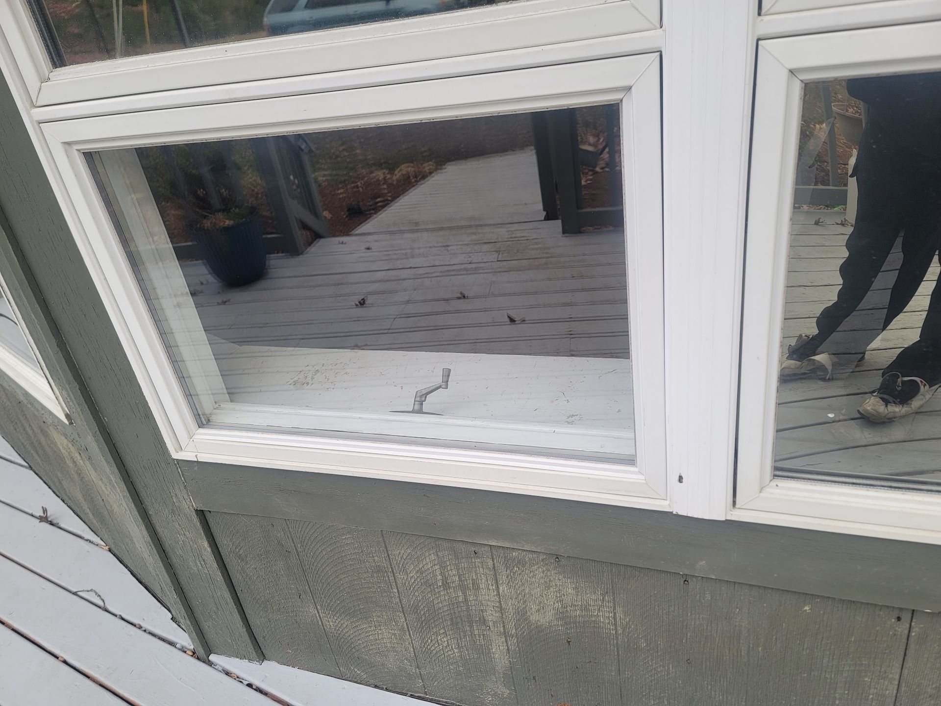 A window with a reflection of a person standing on a deck.
