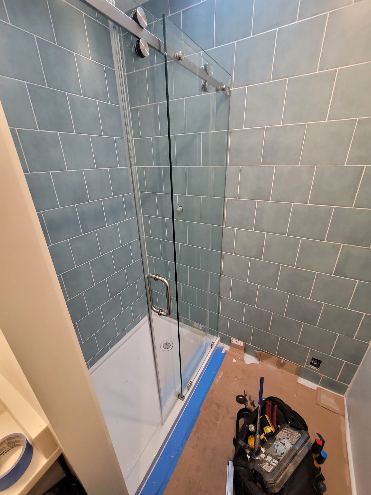 A bathroom with a sliding glass shower door being installed.