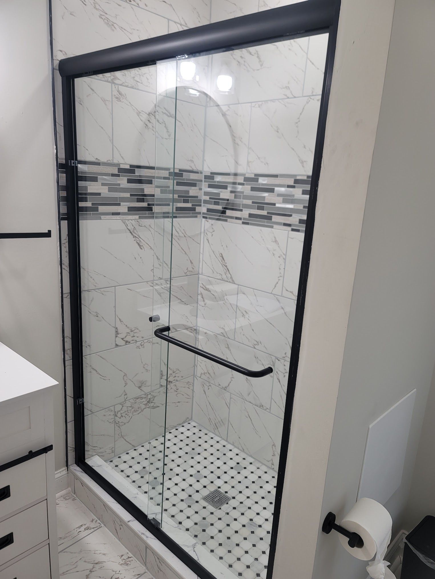 A bathroom with a sliding glass shower door with a black frame.