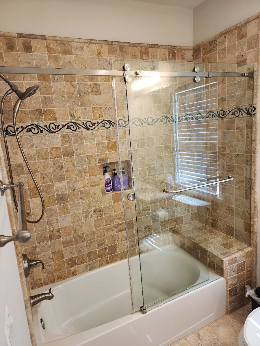 Bathroom with beige tile, glass shower door, and a white bathtub.