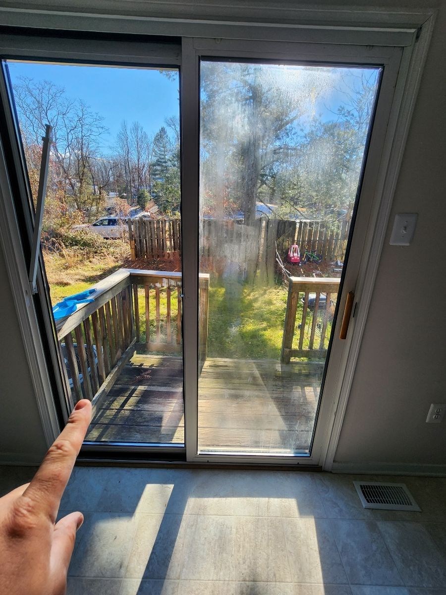 Hand pointing at a sliding glass door. One pane is clear, the other is foggy. A deck and backyard are visible.