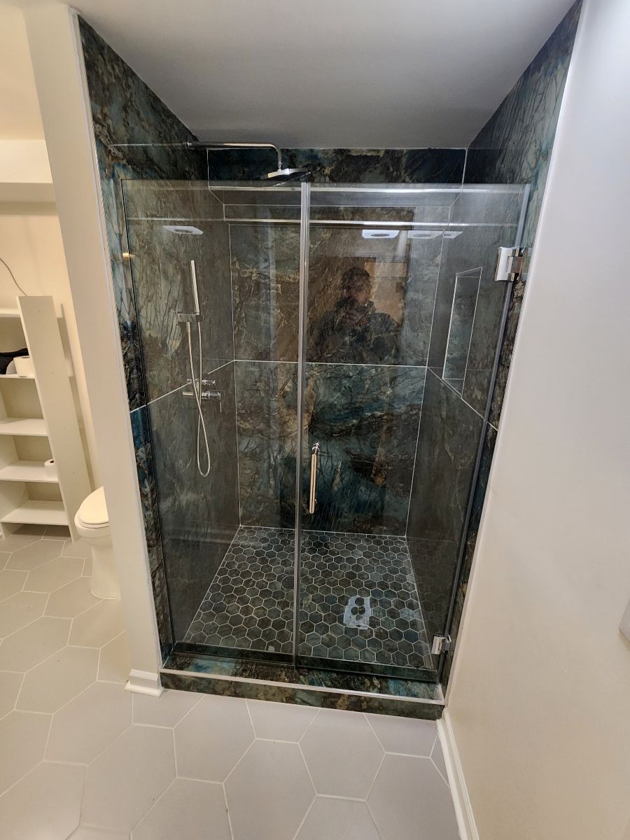 Bathroom shower with dark green stone tile, glass doors, and pebble floor.