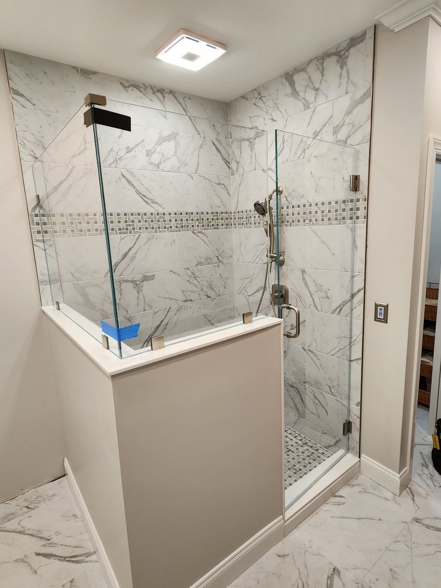 Modern shower stall with marble tile, glass doors, and a partial wall.