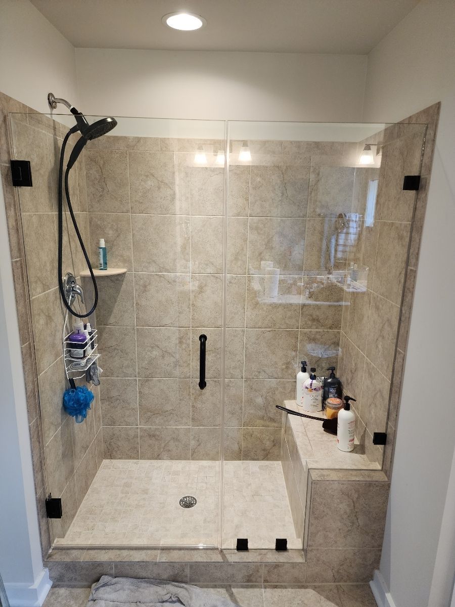 Shower stall with glass doors, tan tile, black fixtures, and built-in bench.