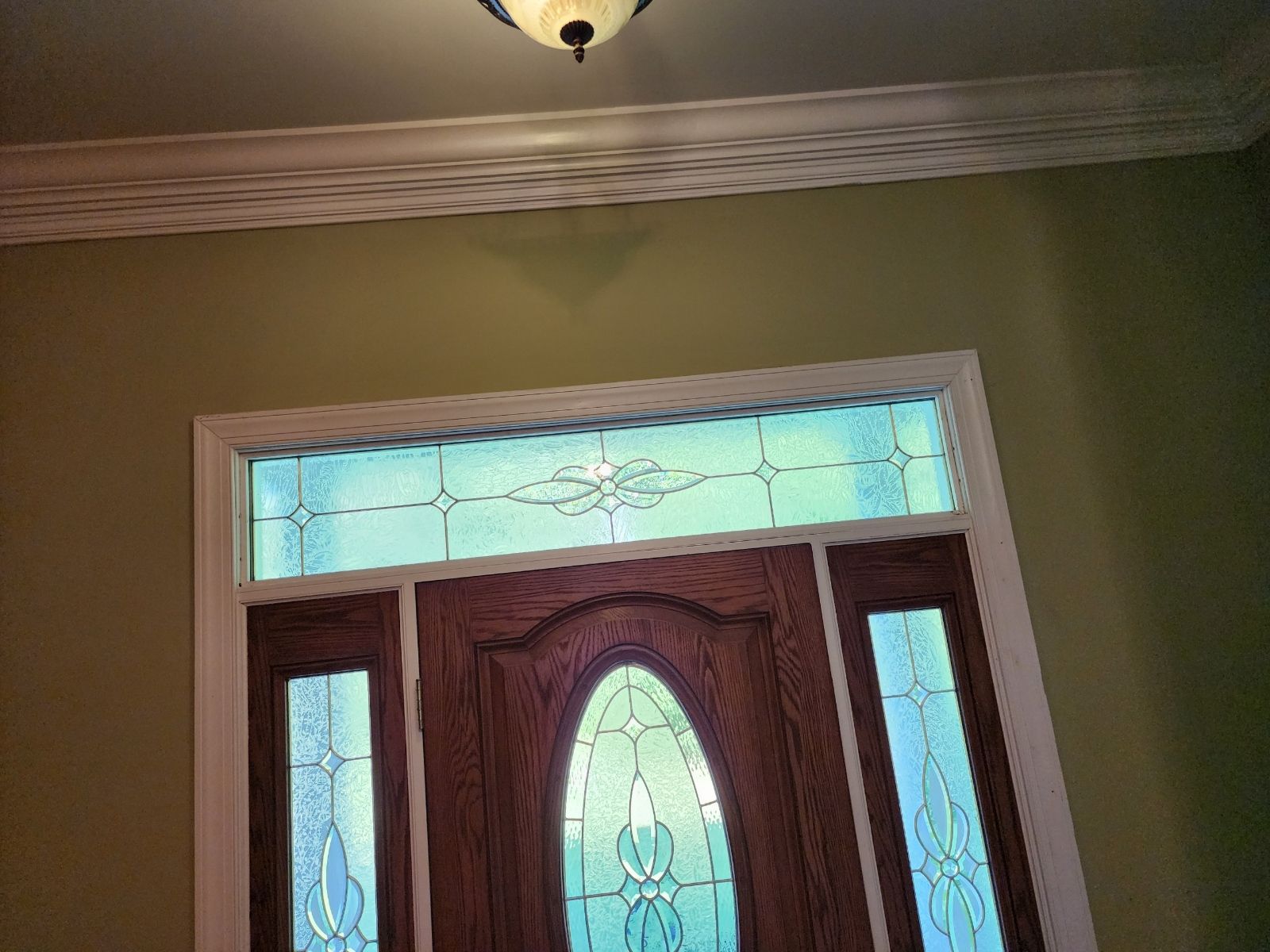Wooden front door with glass panels and sidelights; green walls; decorative ceiling trim.
