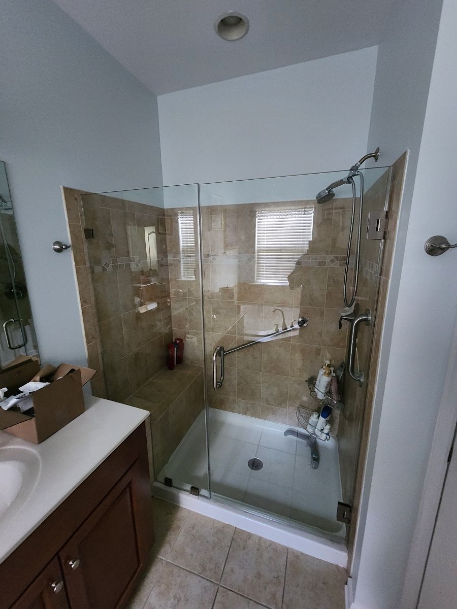 Bathroom with a glass shower, beige tile, and a brown vanity.